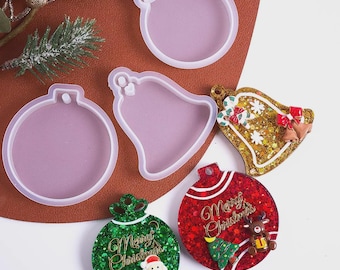 May include: A collection of Christmas ornament molds and finished ornaments. The molds are clear, and the finished ornaments are red, green, and gold with glitter and festive designs, including a Santa, reindeer, and Christmas tree.