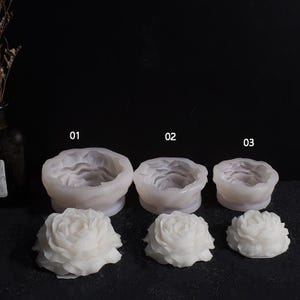 May include: Three white silicone molds in the shape of roses, numbered 01, 02, and 03. Below each mold is a corresponding white rose. The molds are for crafting or casting, and the roses are likely the finished product.