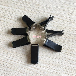 Op de afbeelding: Zeven zwarte metalen autoluchtverfrisserclips. De clips hebben een zilveren afwerking en zijn ontworpen om een kleine luchtverfrisser vast te houden.