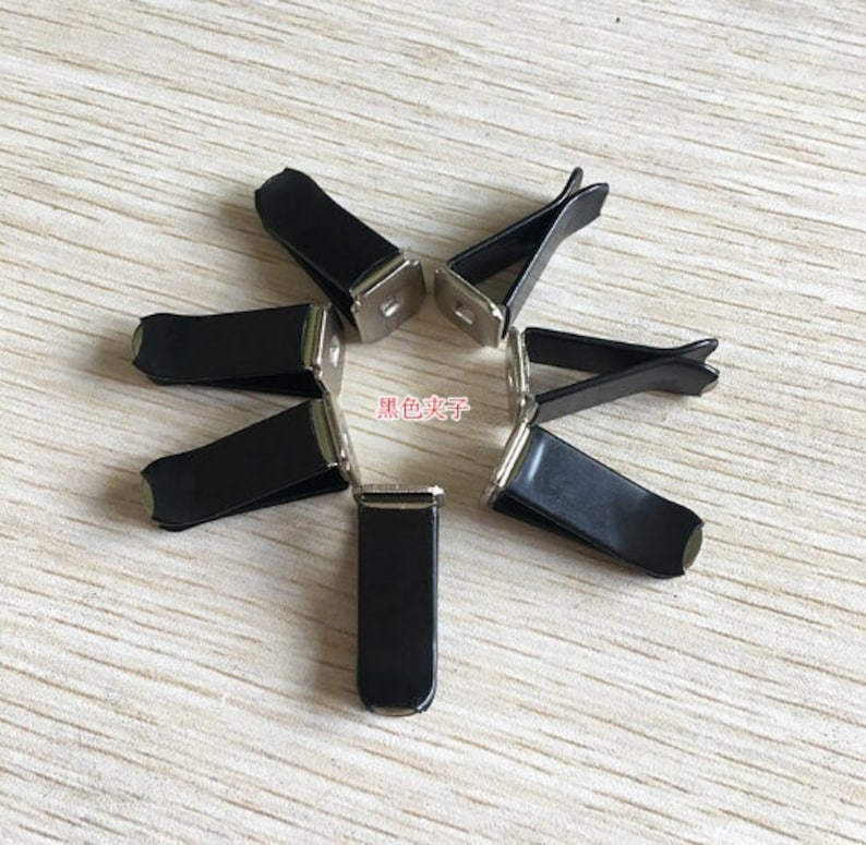 Op de afbeelding: Zeven zwarte metalen autoluchtverfrisserclips. De clips hebben een zilveren afwerking en zijn ontworpen om een kleine luchtverfrisser vast te houden.