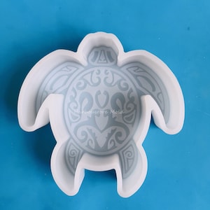 May include: A white silicone mold in the shape of a turtle, featuring a detailed tribal design on its shell. The mold is designed for crafting and creating decorative items. The background is a solid blue.