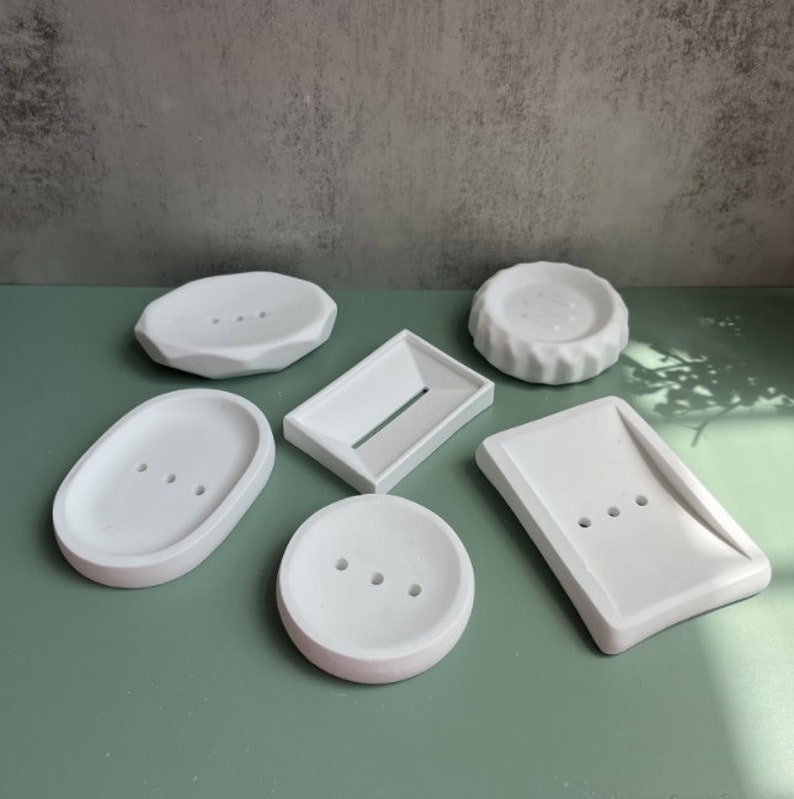 May include: Six white ceramic soap dishes of various shapes and sizes. The dishes have different numbers of drainage holes.