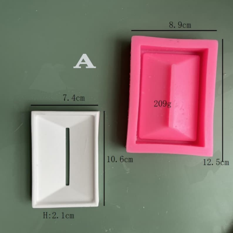May include: A white rectangular soap dish with a raised center and a narrow slot. The dish measures 7.4 inches wide, 10.6 inches long, and 2.1 inches high. A pink silicone mold of the same shape is shown next to it.
