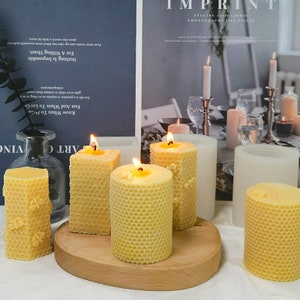 Puede incluir: Cinco velas de panal, cuatro con cera amarilla y una con cera blanca, están dispuestas sobre una superficie de madera. Las velas están encendidas y tienen un brillo cálido. Las velas están rodeadas de un libro blanco con texto sobre "imprint" y "photography".