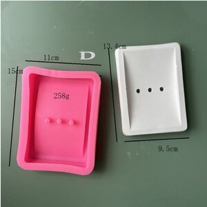 May include: Two silicone molds for making soap bars. The pink mold is 11 cm wide, 15 cm tall, and weighs 258 grams. The white mold is 13.4 cm tall and 9.5 cm wide.