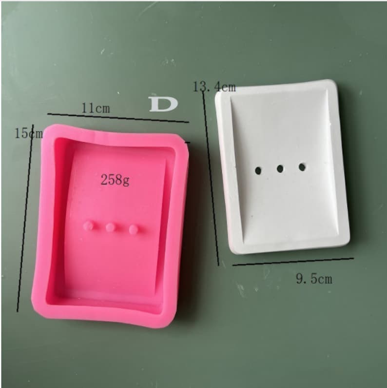 May include: Two silicone molds for making soap bars. The pink mold is 11 cm wide, 15 cm tall, and weighs 258 grams. The white mold is 13.4 cm tall and 9.5 cm wide.