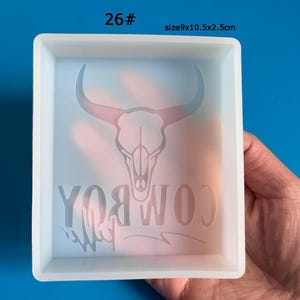 May include: White silicone mold for resin casting. The mold is square and has a raised design of a bull skull with the word "COWBOY" written underneath. The mold measures 9x10.5x2.5 inches.