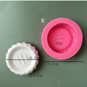 May include: Pink silicone mold for making a round cake or dessert. The mold is 11.7 cm in diameter and has a 10.5 cm diameter circle in the center. The mold is 3.2 cm tall. The mold is labeled "222g".