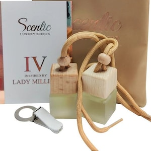 Könnte beinhalten: Zwei kleine Glasflaschen mit Holzdeckeln und einem beigefarbenen Kordelbeutel. Die Flaschen sind mit einer klaren Flüssigkeit gefüllt und haben jeweils eine goldene Schnur. Die Flaschen sind mit "Scentic Luxury Scents IV Inspired by Lady Milli" beschriftet.