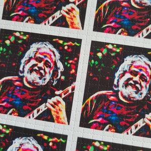 May include: A psychedelic image of a person playing a guitar. The image is made up of small squares of different colors, creating a mosaic effect. The person's face is obscured by the squares, but their hair and guitar are visible. The background is black.