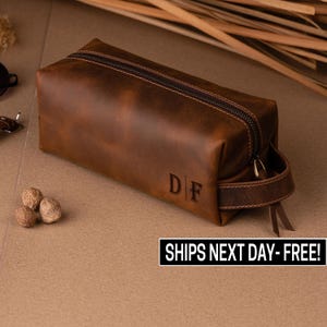 May include: A brown leather travel toiletry bag with a zipper closure and a leather handle. The bag has the initials "D|F" embossed on the front.