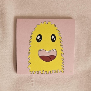 Peut inclure: Une carte carrée rose représentant un monstre de dessin animé avec un corps jaune, des yeux noirs et une bouche grande ouverte. Le monstre a un contour dentelé et une langue rouge. Le fond est de couleur rose clair.