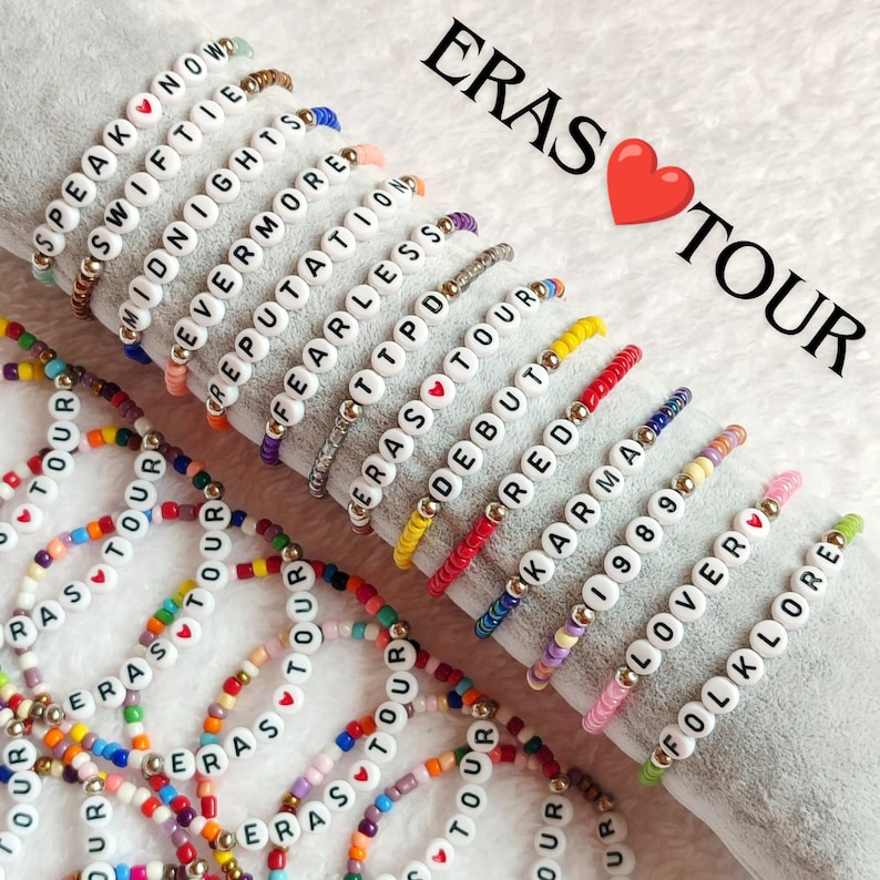 May include: A collection of colorful beaded bracelets with white beads spelling out the names of Taylor Swift's albums, including "Speak Now", "Midnights", "Evermore", "Reputation", "Fearless", "Eras Tour", "Debut", "Red", "Karma", "1989", "Lover", and "Folklore".
