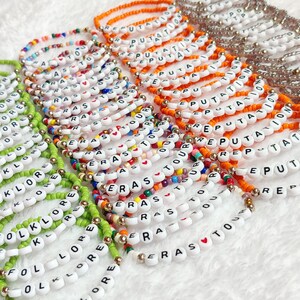 May include: A collection of colorful beaded bracelets with different words spelled out on them, including "Reputation", "Eras", "Tour", "Folklore", and "Lore".
