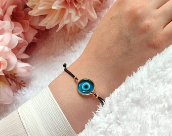 May include: A black string bracelet with a gold-rimmed blue evil eye charm.