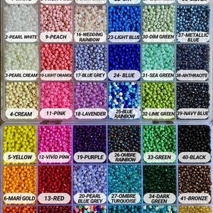 May include: A clear plastic organizer filled with small, colorful beads. The beads are arranged in labeled compartments, showcasing a variety of colors including white, pink, blue, green, and gold. The labels include the color names and numbers.