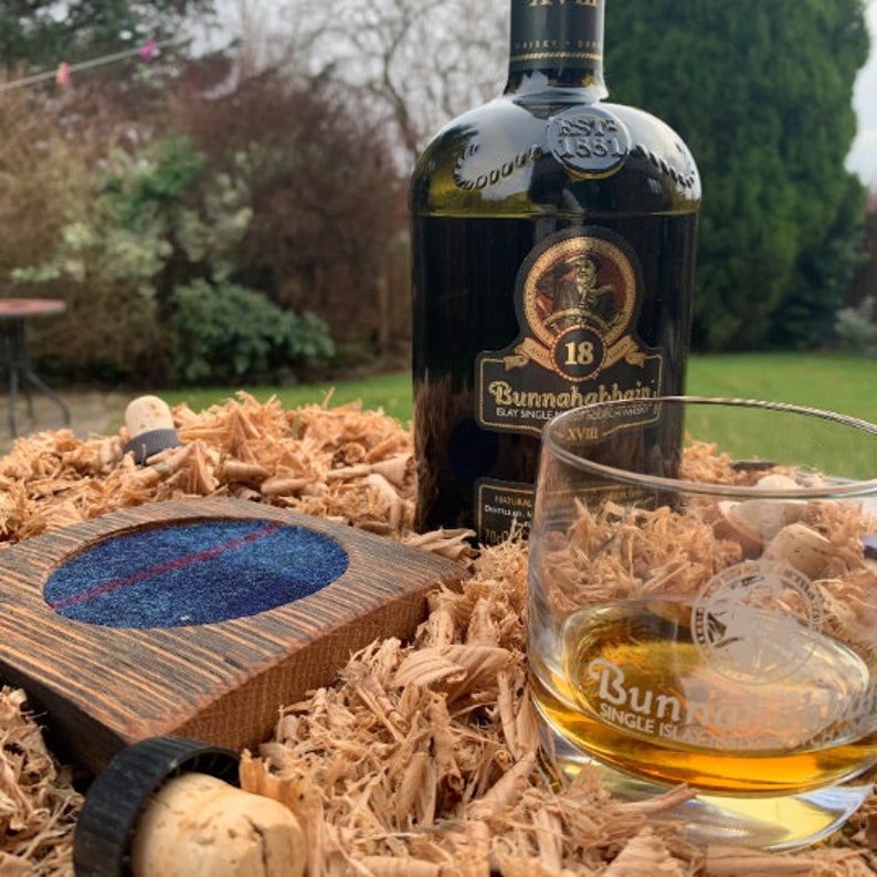 Pode incluir: Um copo de whisky escoc&ecirc;s de malte &uacute;nico Bunnahabhain de cor &acirc;mbar num copo transparente com um logotipo Bunnahabhain no fundo. Uma garrafa de whisky escoc&ecirc;s de malte &uacute;nico Bunnahabhain de 18 anos est&aacute; no fundo. A garrafa e o copo est&atilde;o sobre uma cama de aparas de madeira.