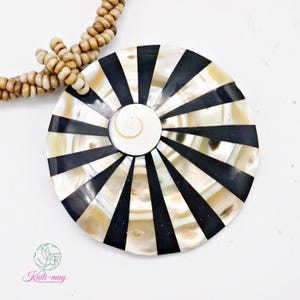 May include: A necklace featuring a large, circular pendant made of alternating black and iridescent white shell segments arranged in a sunburst pattern, with a central spiral shell piece and a strand of small, light brown wooden beads.