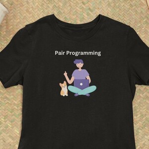 Könnte beinhalten: Schwarzes T-Shirt mit einem Grafikdruck einer Person, die mit einem Laptop und einem Hund sitzt. Der Text "Pair Programming" befindet sich über dem Grafikdruck.