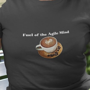 Puede incluir: Una camiseta gris oscuro con el texto "Fuel of the Agile Mind" y un gráfico de una taza de café con un diseño de corazón en la espuma.