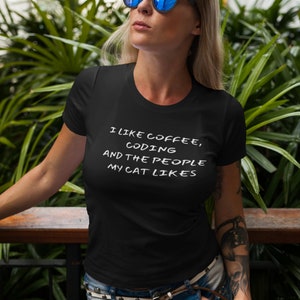May include: A woman wearing a black t-shirt with the text "I like coffee, coding and the people my cat likes" printed in white. She is wearing blue jeans and sunglasses.