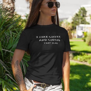 Puede incluir: Una mujer con una camiseta negra con el texto "Me gusta el café y la codificación, eso es todo" en blanco. Lleva pantalones cortos de mezclilla y gafas de sol.