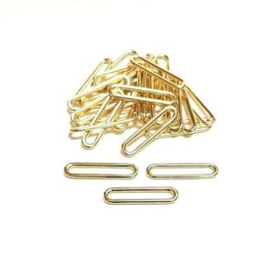 May include: A pile of gold-coloured metal oval rings, with three more rings laid out separately on a white surface.