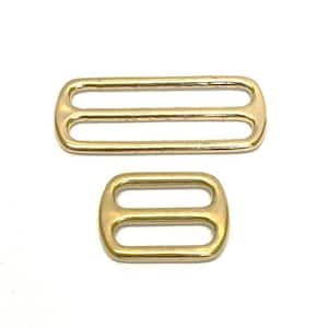 May include: Two gold metal slider buckles. The larger buckle has two slots and the smaller buckle has one slot.