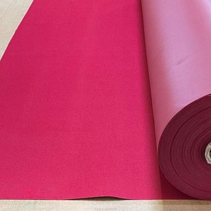 May include: A roll of deep red fabric, unfurled on a light brown surface. The fabric is smooth and has a slight sheen.