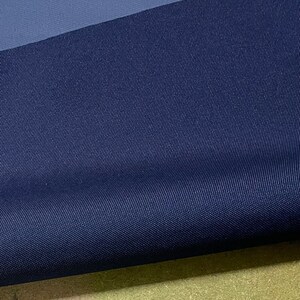 May include: A close-up of a dark blue fabric with a subtle textured pattern. The fabric is folded in half, revealing a lighter blue underside.