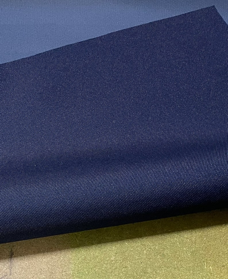 May include: A close-up of a dark blue fabric with a subtle textured pattern. The fabric is folded in half, revealing a lighter blue underside.