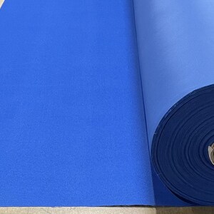 May include: A roll of bright blue fabric, unfurled on a brown surface. The fabric is smooth and appears to be a woven material.