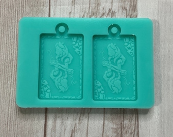 May include: A teal silicone mold with two rectangular cavities. Each cavity features a raised design of two figures holding hands, surrounded by intricate floral patterns.