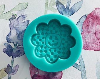 May include: A turquoise silicone mold with a checkered flower design and a jack-o'-lantern face in the center.