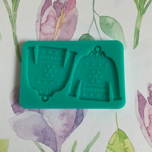 May include: Green silicone mold with two Christmas sweater shapes. The sweaters have a snowflake and a geometric pattern.