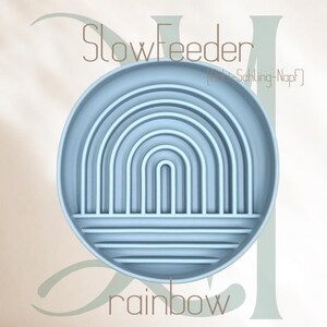 May include: A light blue silicone slow feeder dish shaped like a rainbow. The dish has multiple compartments and ridges to slow down eating. The text "Slow Feeder" and "[Slow-Schluing-Napf]" is printed on the dish. The text "rainbow" is printed below the dish.