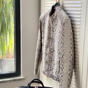 以下が含まれることがあります： ヘビ革のジャケットと、黒いアクセントの付いたヘビ革のブリーフケース