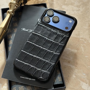 May include: Black textured phone case with a crocodile skin pattern. The case is on a black box with a card that says "Thank You". The phone case has a blue back and three camera lenses. The website address www.mhiraje.com is visible.