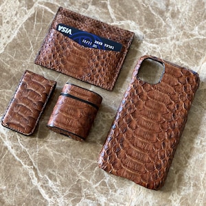 Könnte beinhalten: Ein Set brauner Lederaccessoires, darunter ein Kartenhalter mit einer Visa-Karte, eine Handyhülle, ein Feuerzeug-Etui und ein kleines Etui. Die Artikel haben ein strukturiertes, reptilienartiges Muster.