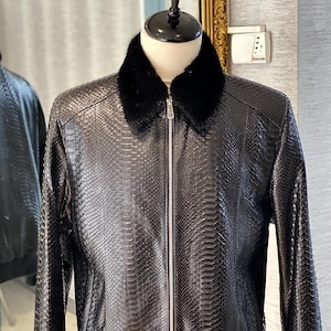 Może przedstawiać: Czarna skórzana kurtka bomberowa z kołnierzem z futra. Kurtka jest wykonana ze skóry węża.