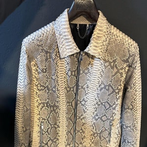 Może przedstawiać: Beżowa skórzana kurtka ze skóry węża z zamkiem błyskawicznym. Kurtka ma stójkę i długie rękawy.