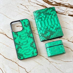May include: A set of green snake-skin textured accessories, including a phone case, a wallet, and a small rectangular case, possibly for earbuds. The items are arranged on a marble surface.