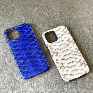 May include: Two phone cases with a reptile skin pattern. One case is a vibrant blue, and the other is off-white with gray tones. The cases have cutouts for the camera and buttons.