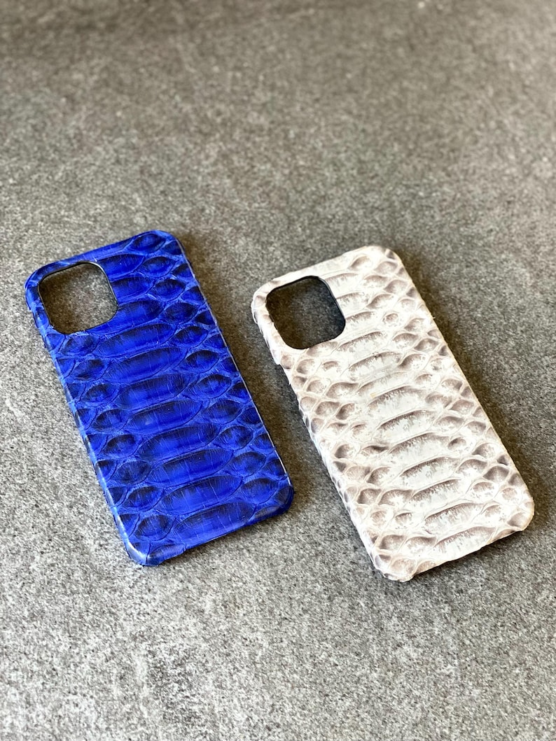 May include: Two phone cases with a reptile skin pattern. One case is a vibrant blue, and the other is off-white with gray tones. The cases have cutouts for the camera and buttons.