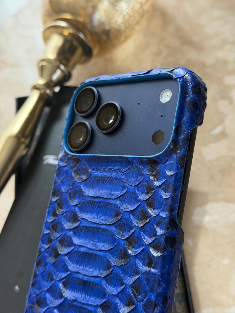 May include: A blue snakeskin-textured phone case with a black camera module. The case has a textured, scaly pattern in shades of blue and black. The phone case is designed to fit a smartphone.