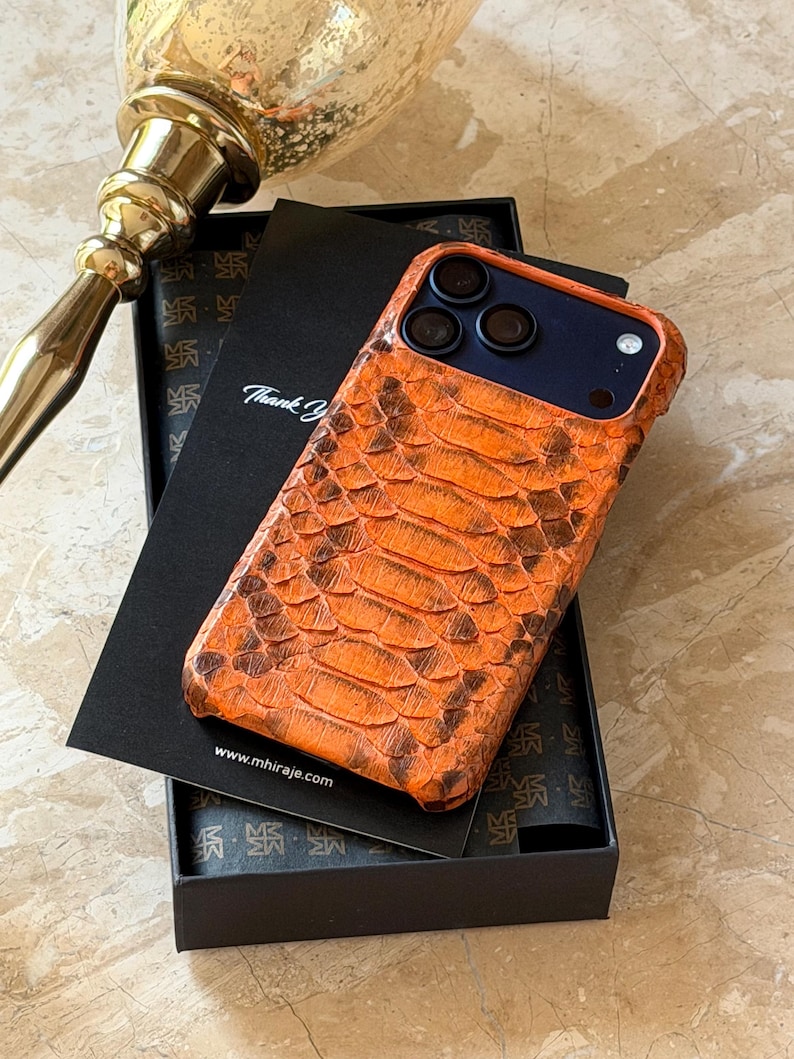 May include: Orange and brown snakeskin-textured phone case with a dark blue interior. The case is displayed in a black box with a thank you card. The website address www.mhiraje.com is visible on the card.