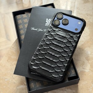 May include: Black textured phone case with a scale-like pattern, displayed on a black box with the text "Thank You". The phone case has a blue camera module and is shown with a matching patterned interior.