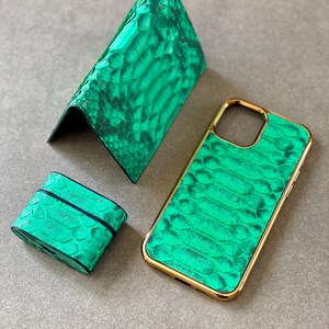 May include: A set of green leather accessories, including a wallet, phone case, and a small case, likely for earbuds. The items have a textured, snake-skin-like pattern and gold-colored trim on the phone case.