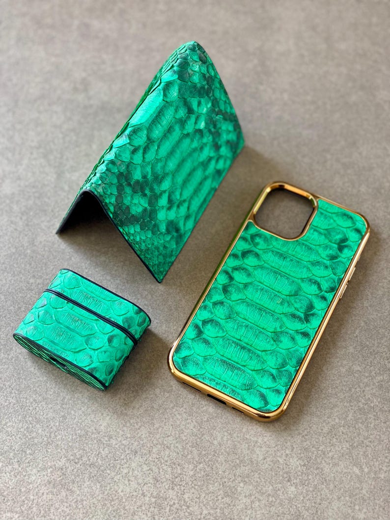 May include: A set of green leather accessories, including a wallet, phone case, and a small case, likely for earbuds. The items have a textured, snake-skin-like pattern and gold-colored trim on the phone case.