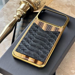 Op de afbeelding: Een goudkleurige iPhone-hoes met een zwart, slangenhuid-achtig achterpaneel. De hoes heeft een gouden frame en verticale gouden strepen. De tekst "24k Gold Python Edition" staat onderaan.